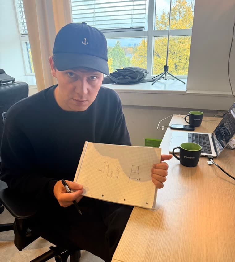 Ott at his desk, holding a notebook sketch of a 4.2 m chair next to a stick figure